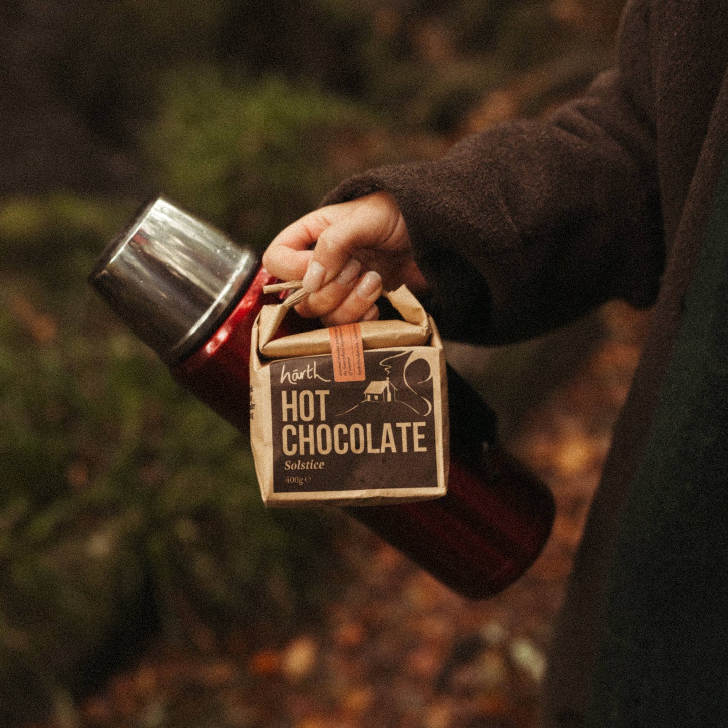 Person holding a container of hot chocolate in a forest setting