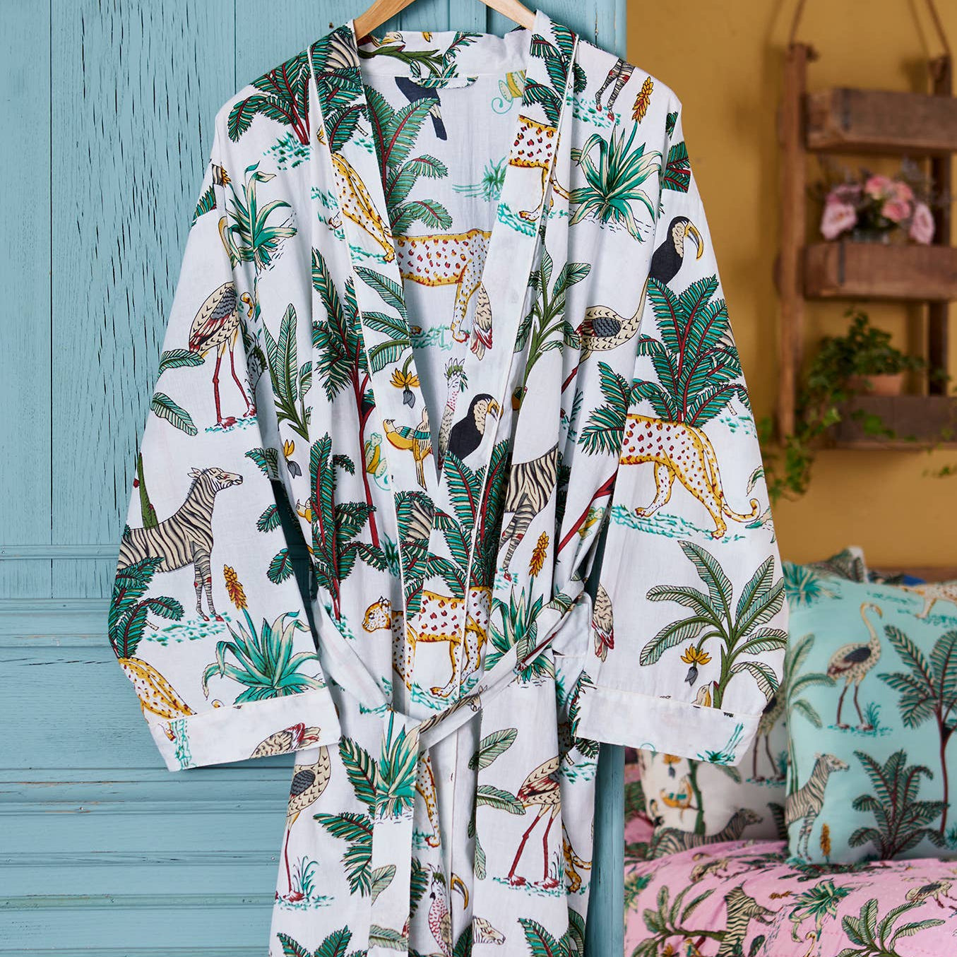 A white dressing gown with a colorful jungle print including plants and animals, displayed in a room with wooden furniture and a pink rug.