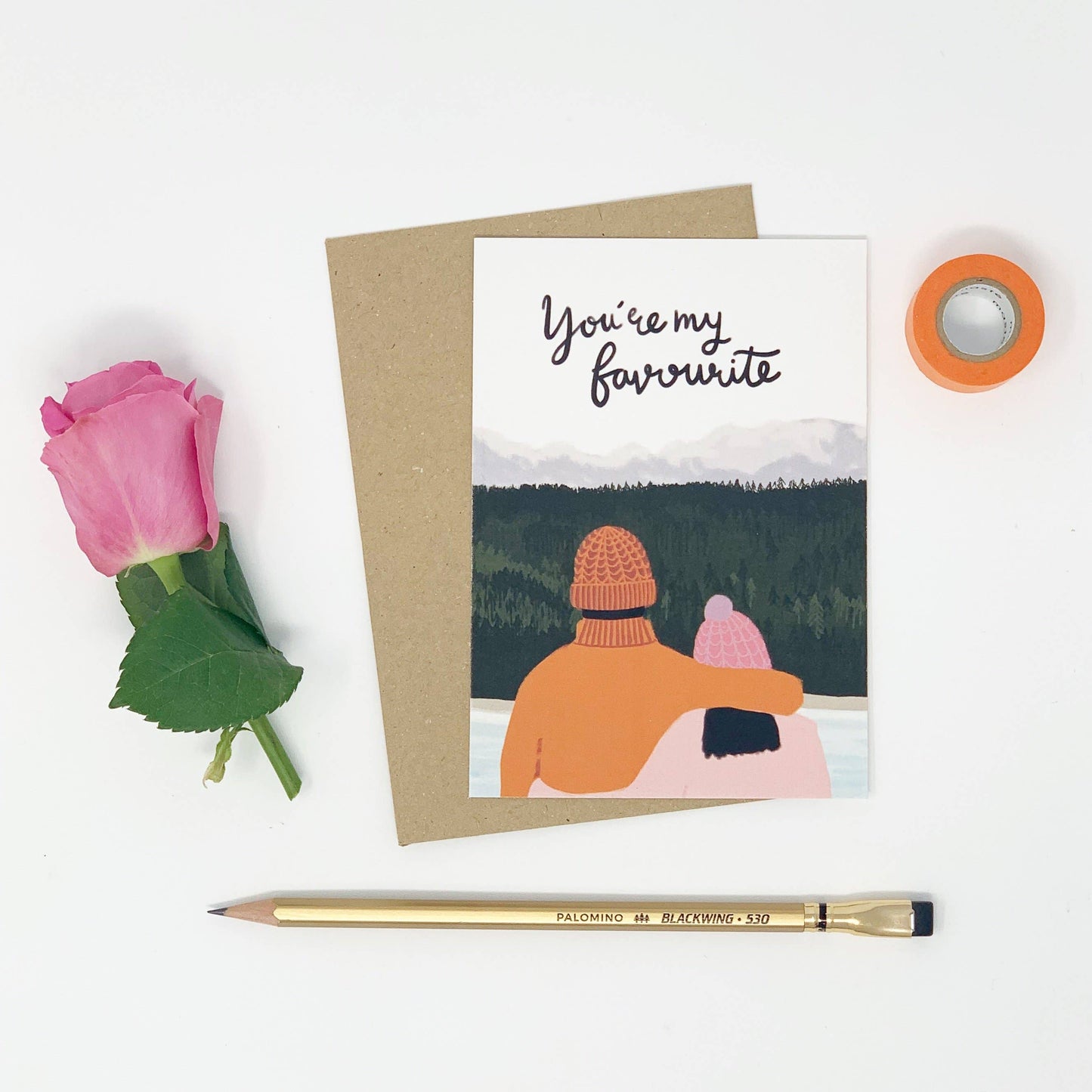 Greeting card with illustration of two people in winter hats, pink rose, and pen on white background