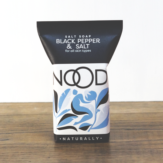 A bar of soap with black and blue packaging labeled 'NOOD Salt Soap Black Pepper & Salt' for all skin types.
