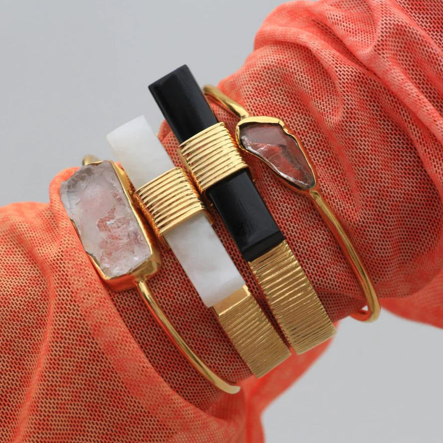 Gold and black bracelet on a wrist with a red sleeve against a gray background