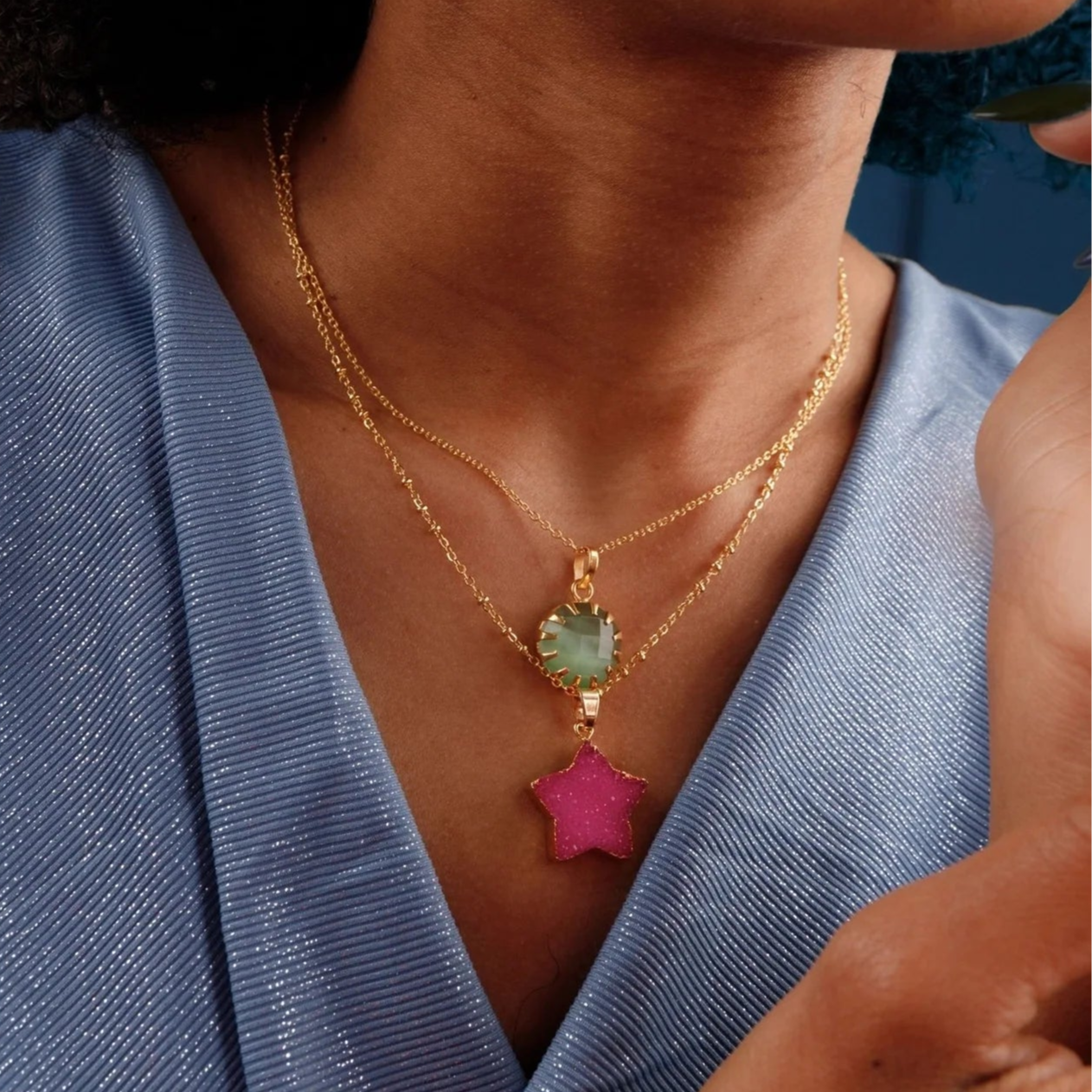 Woman wearing a blue top with gold and pink necklace against a blue background