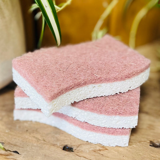 Stack of pink and white sponges on a wooden surface with a blurred plant background