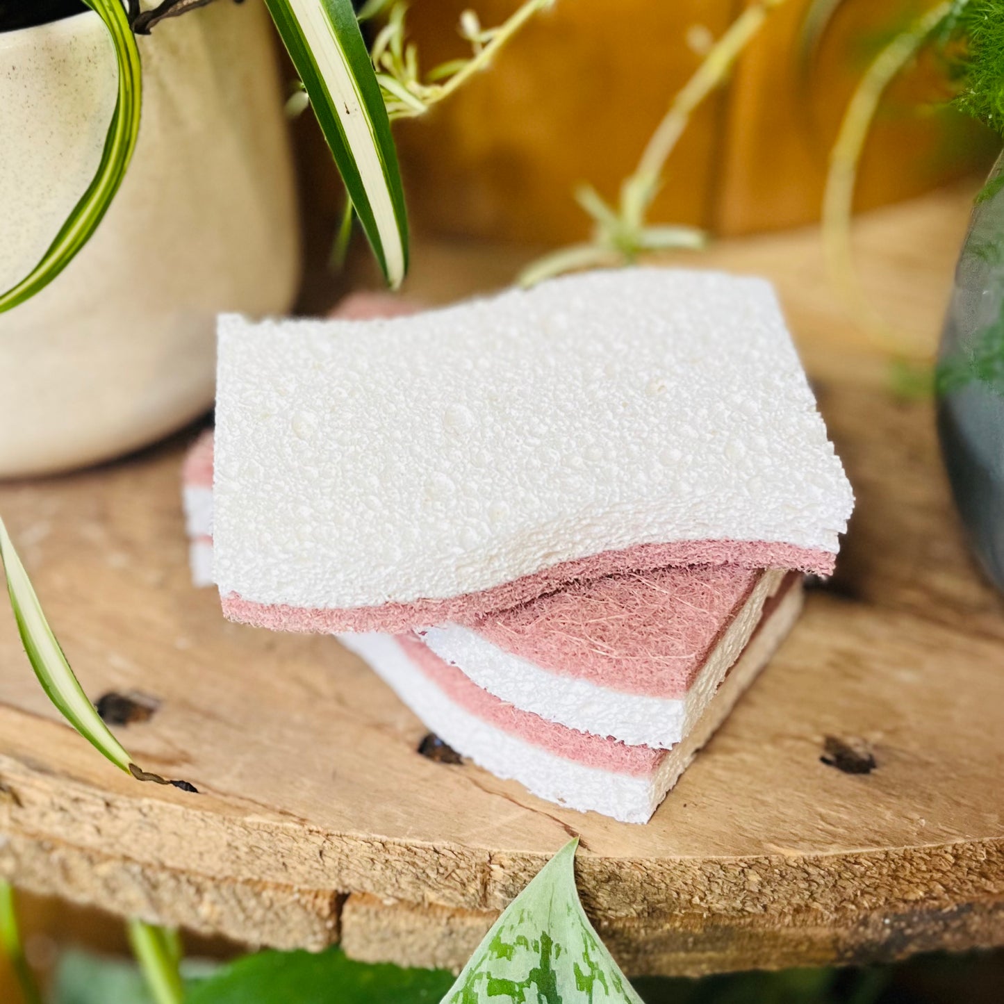 Stack of pink and white cloths on a wooden surface with plants in the background