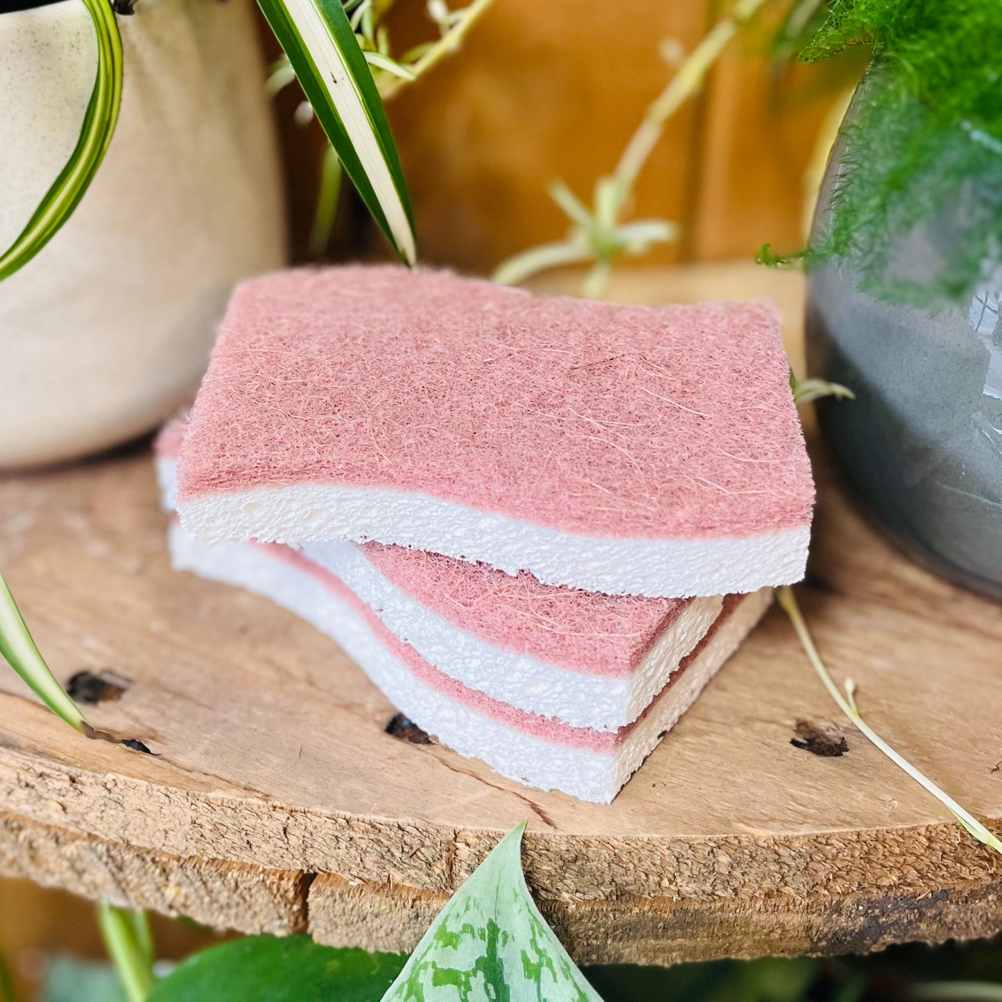 Stack of pink and white cloths on a wooden surface with plants in the background