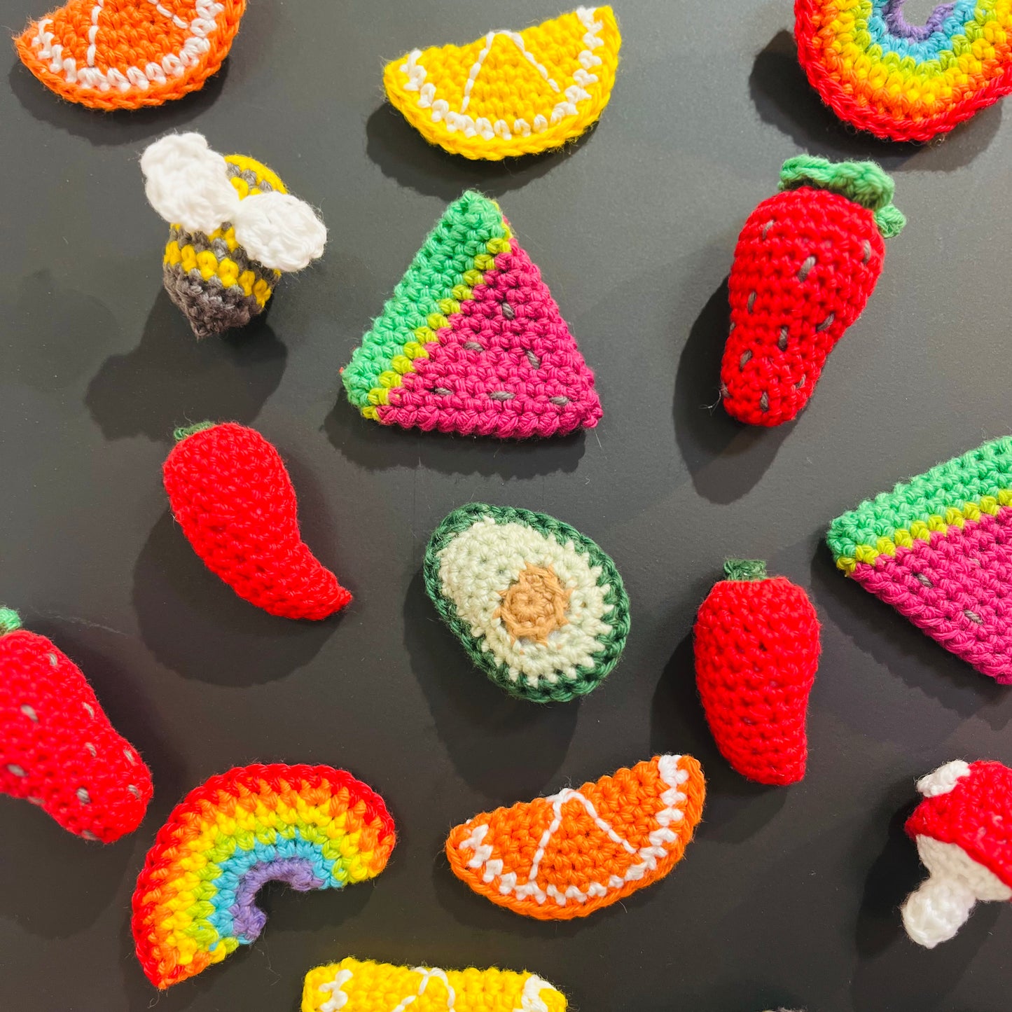 Colorful crochet fruits and vegetables on a dark surface