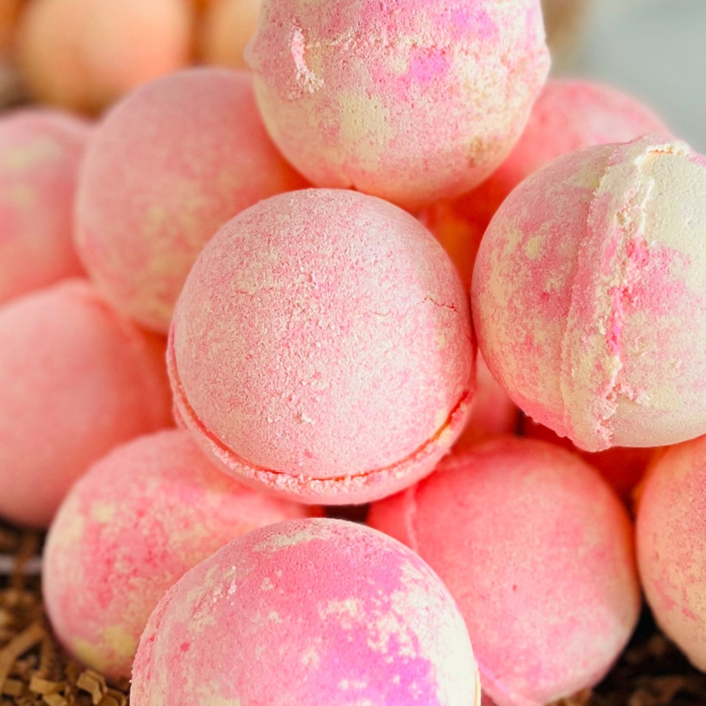 A bunch of Pink Lemonade bath bombs, a gentle orange and pink colour, sat on a bed of crinkled brown paper.