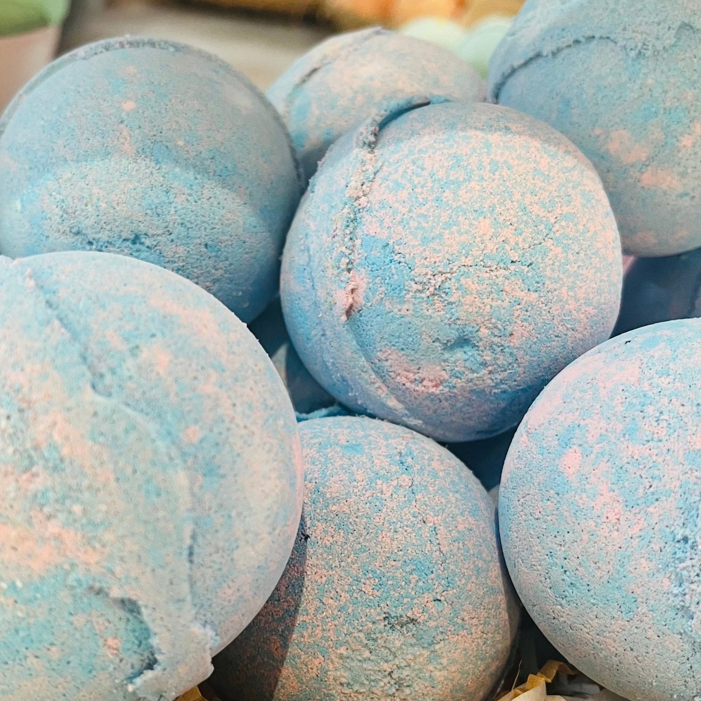 Multiple baby powder fragranced bath bombs, piled up. They are a soft blue and pink colour.