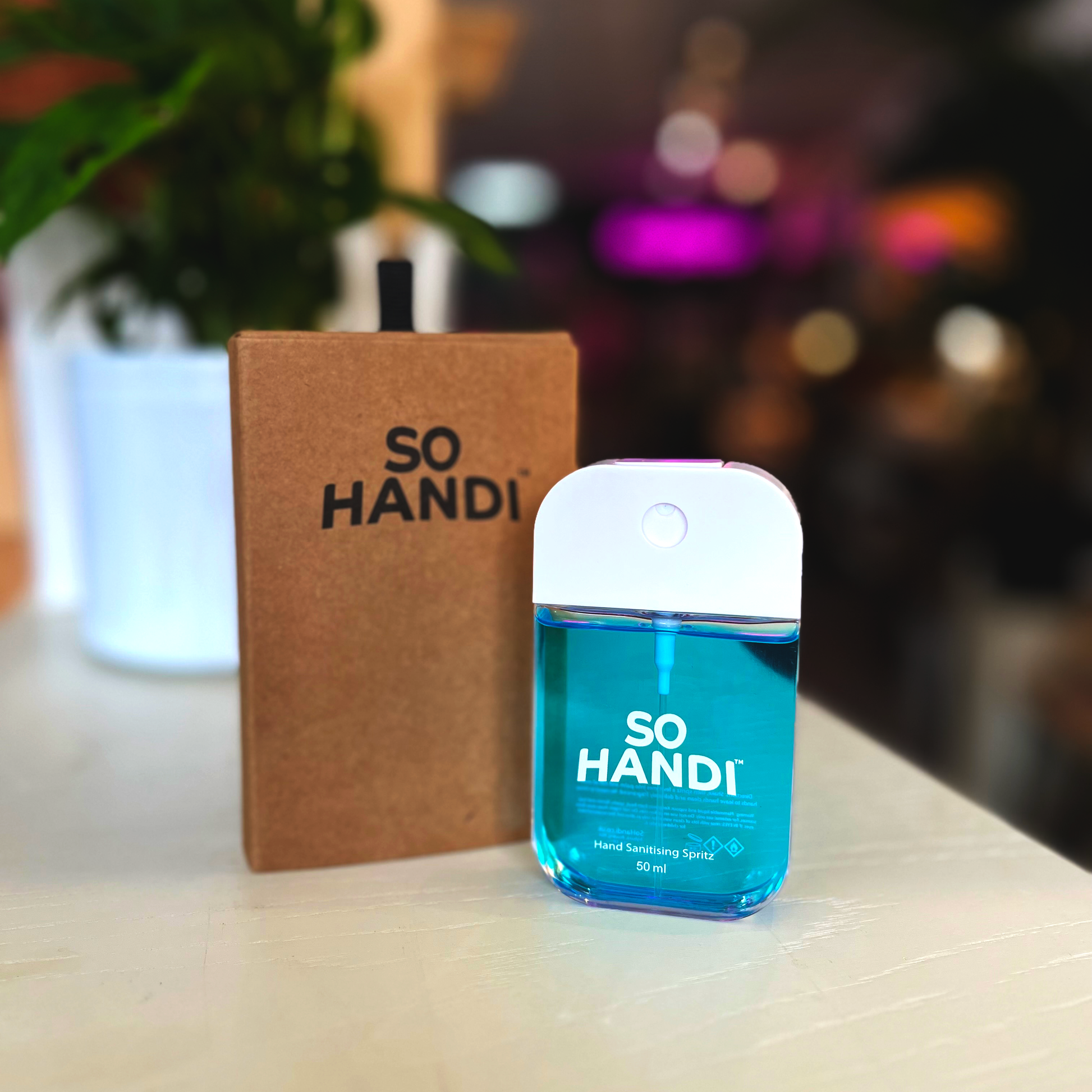 A spritzer bottle of blue hand sanitiser, placed in front of its recyclable packaging.