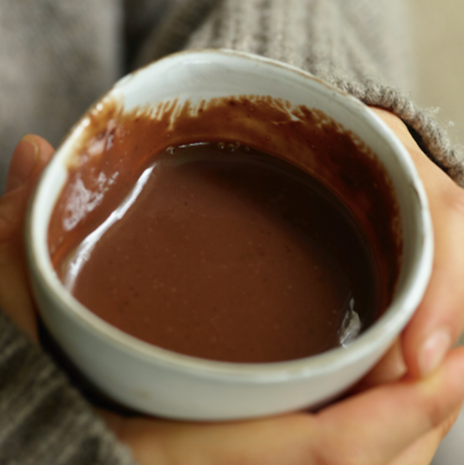 Person holding a small white bowl filled with a brown liquid, possibly hot chocolate.
