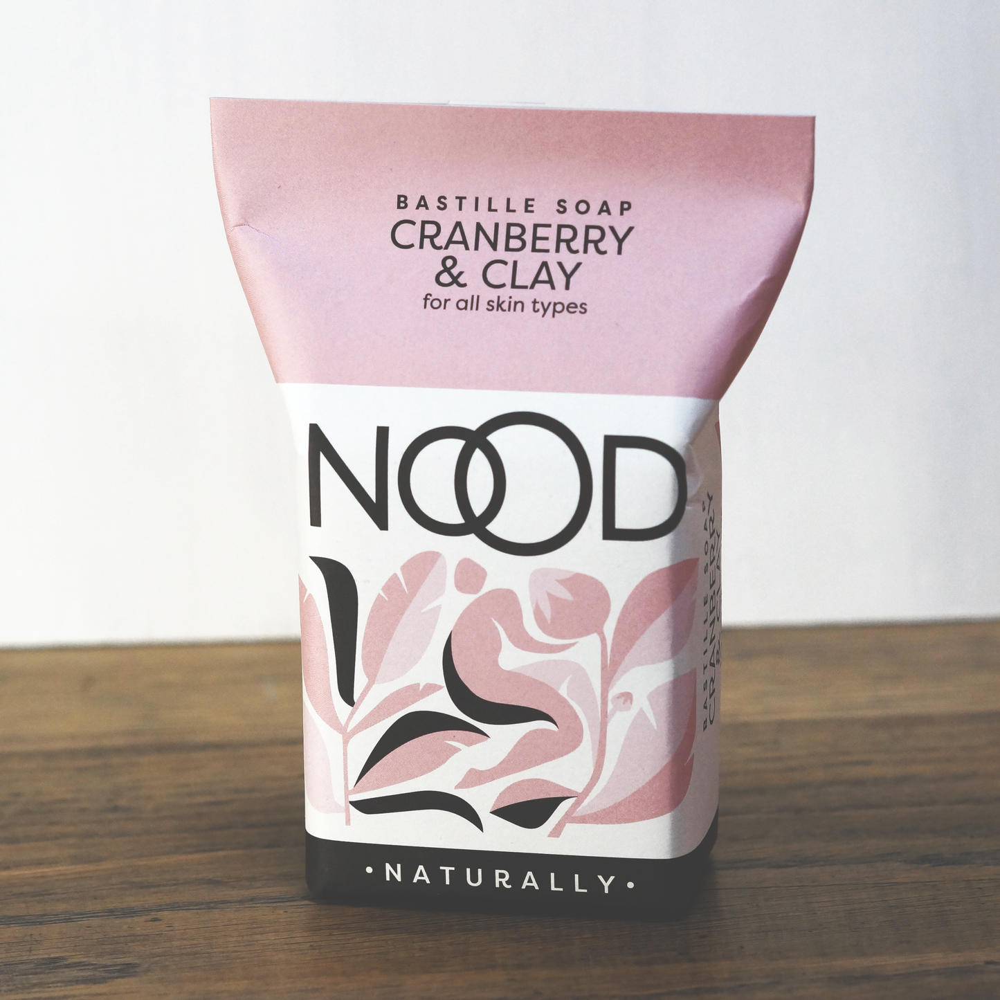Packaged bar soap with 'NOOD' branding, 'CRANBERRY & CLAY' label, and 'NATURALLY' text, indicating it's for all skin types.