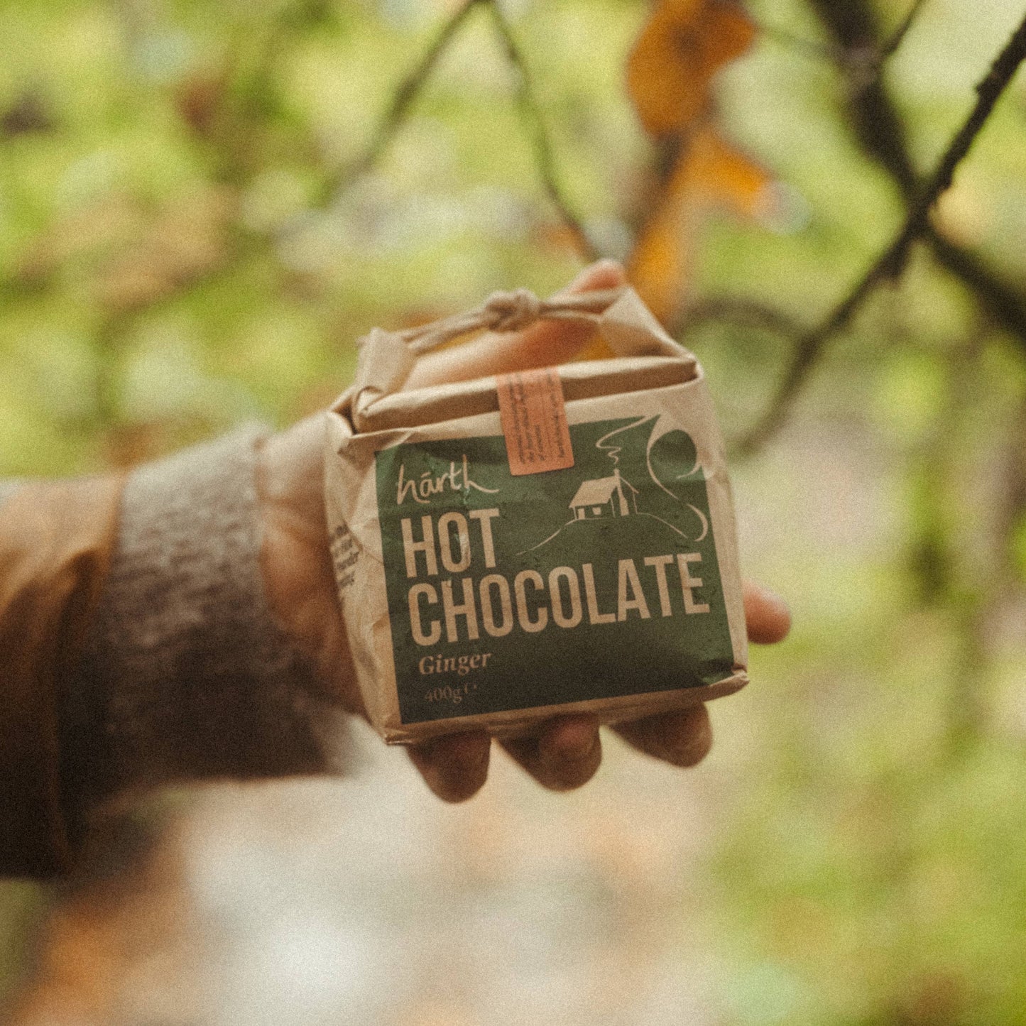 Hand holding a package of hot chocolate in a forest setting