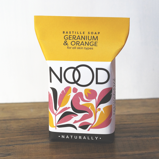A bar of geranium & orange soap, wrapped in recyclable orange, pink, white and black packaging. With the branding 'NOOD Naturally' which suggests it's made by NOOD Stores.