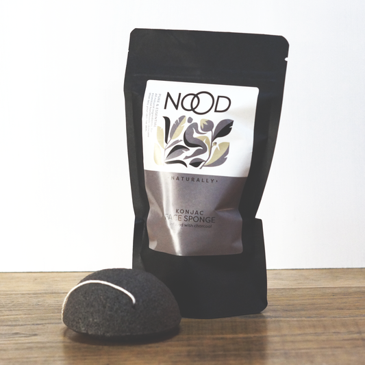 Neat black packaging containing a charcoal-infused konjac sponge from NOOD Stores, with a charcoal konjac laid in front of it.