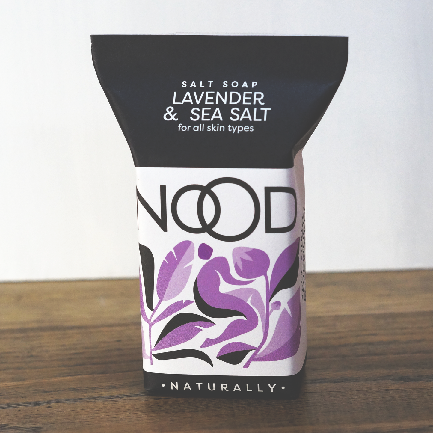A bar of Lavender & Dead Sea Salt Soap with packaging that includes purple and black colors with floral and leaf patterns.