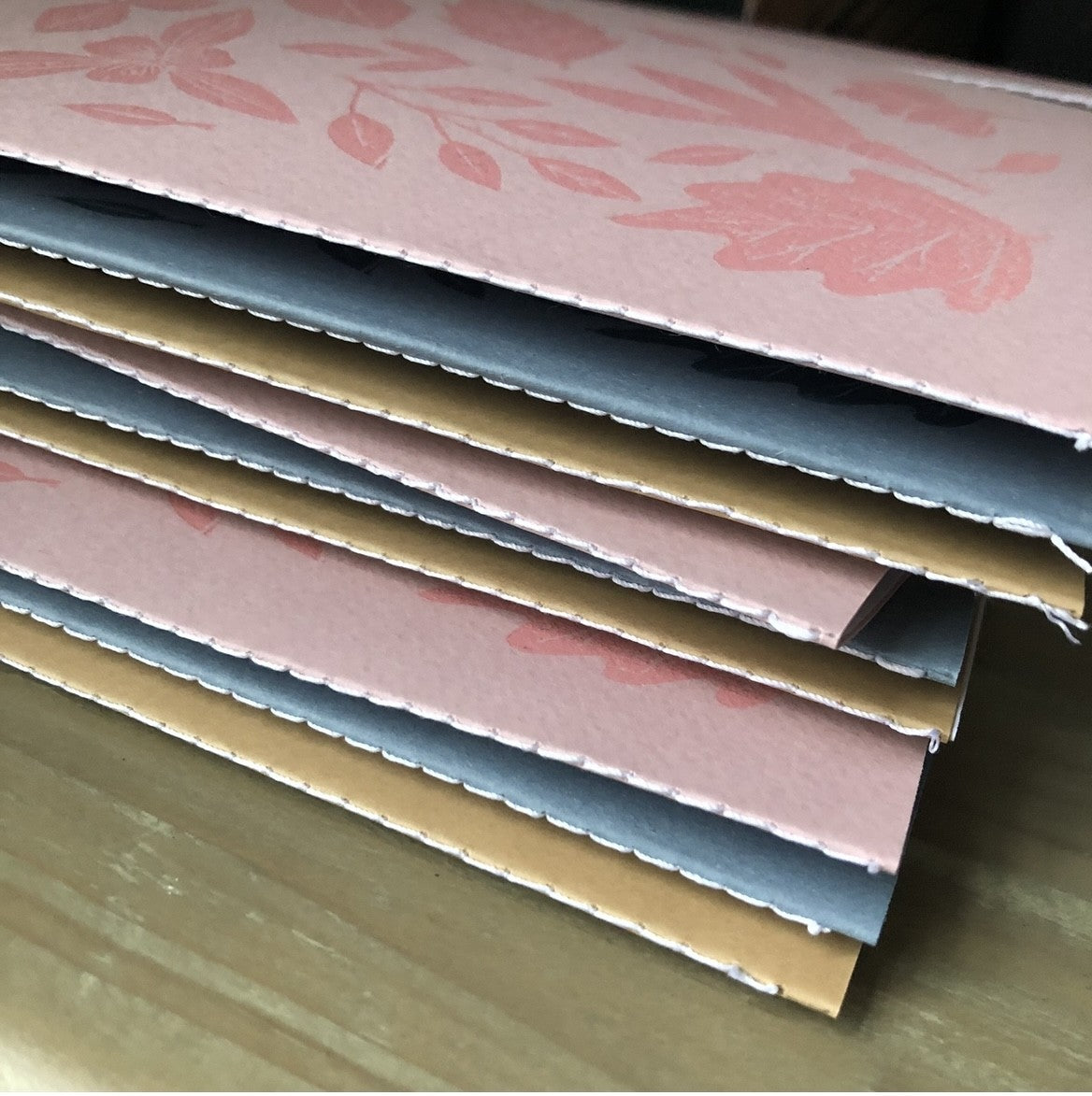 Stack of colorful paper samples with floral patterns on a wooden surface