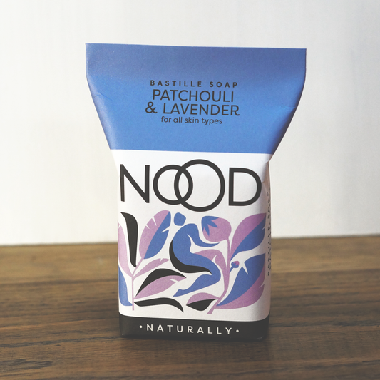 A packaged bar of bastille soap, patchouli and lavender fragrance - the packaging is blue, purple, white and black. With the branding 'NOOD' on it.