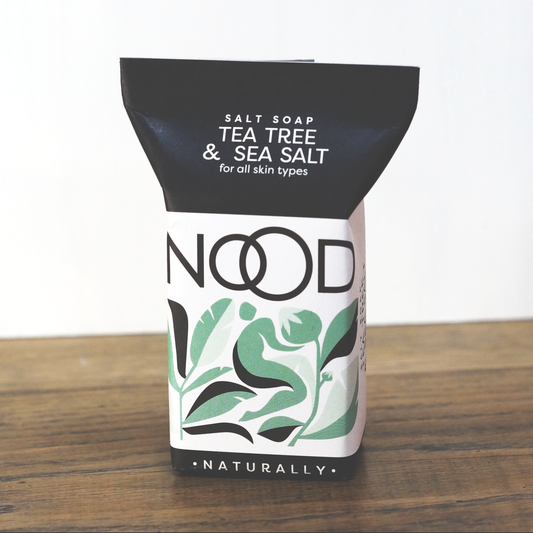 A bar of Tea Tree & Dead Sea Salt Soap packaged in a black and green wrapper with the brand 'NOOD' prominently displayed. The packaging also features the text 'Salt Soap', 'Tea Tree & Sea Salt', and 'for all skin types'.