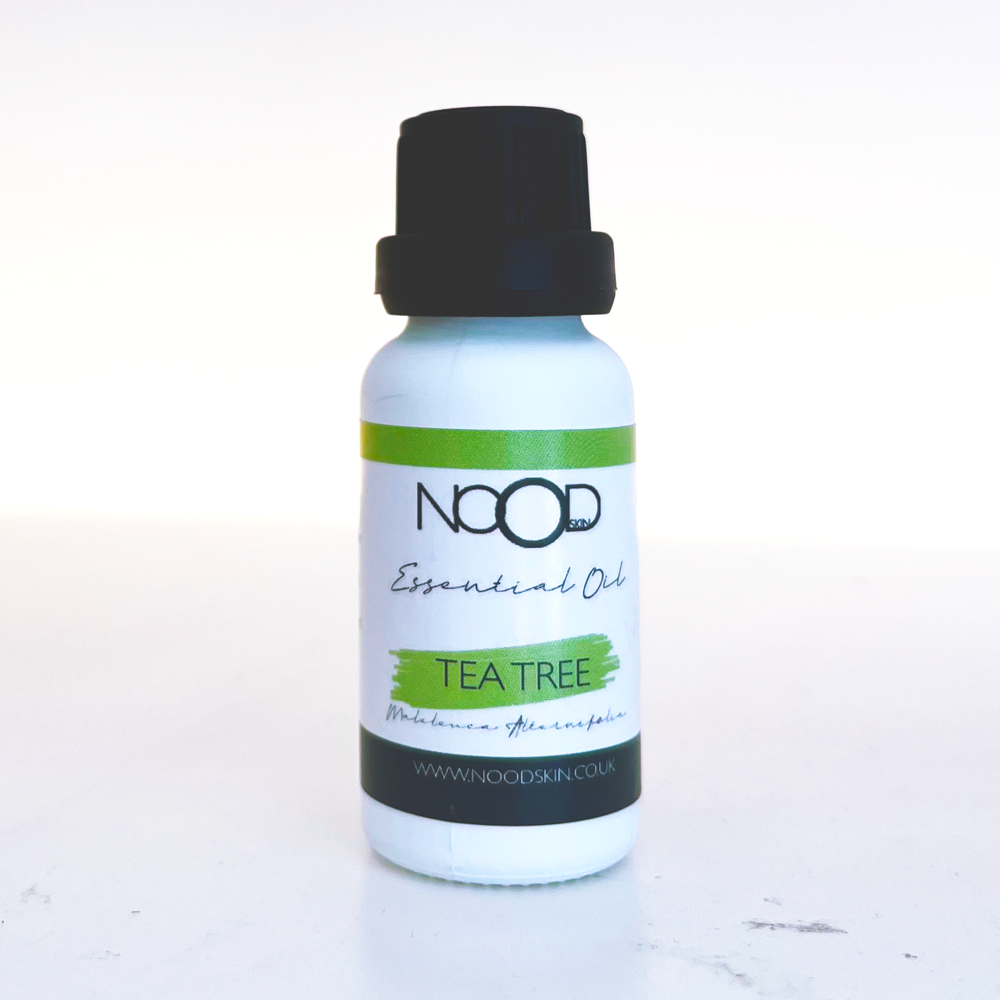 A small white bottle with a screw-top lid and the words 'NOOD skin' Essential Oil, with a green stripe that has 'TEA TREE' written in thin black font.