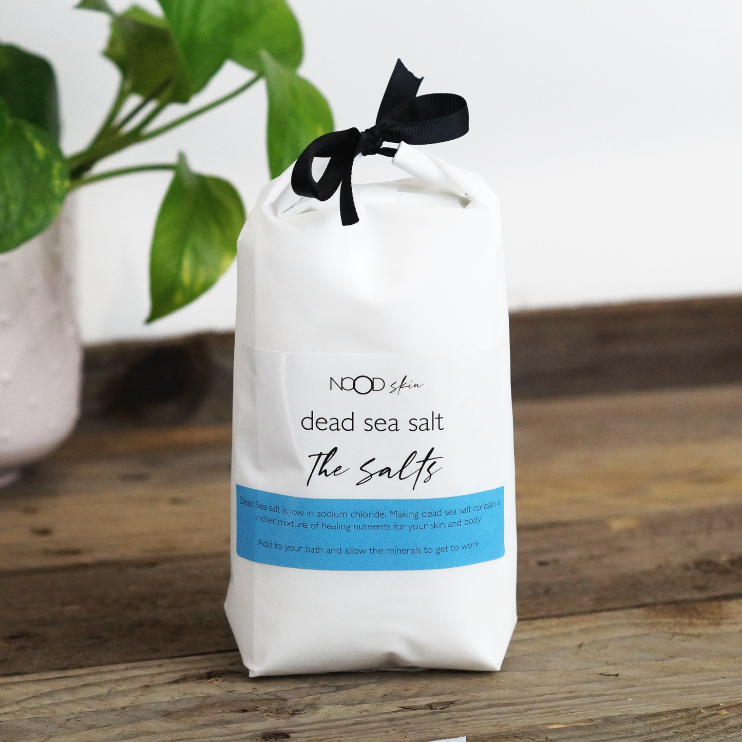 A resealable white plastic bag labeled 'NOOD Dead Sea Salt' containing 1kg of bath salts, with a black ribbon on the top and a blue accent on the label.