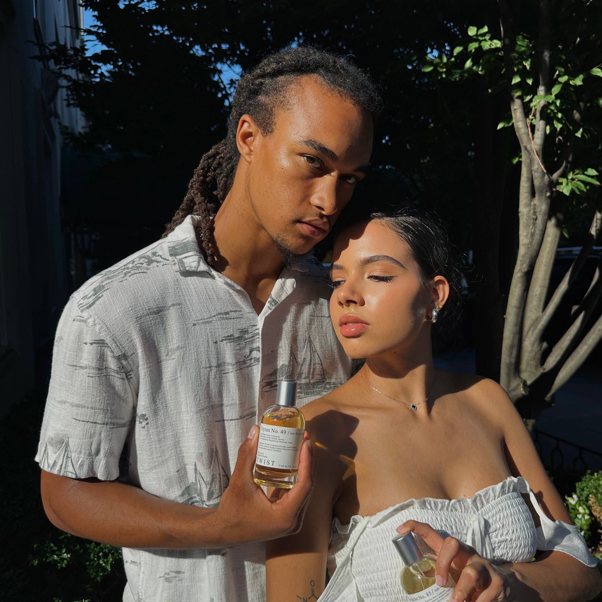 Two people outdoors, one holding a bottle of oil, with a natural background.