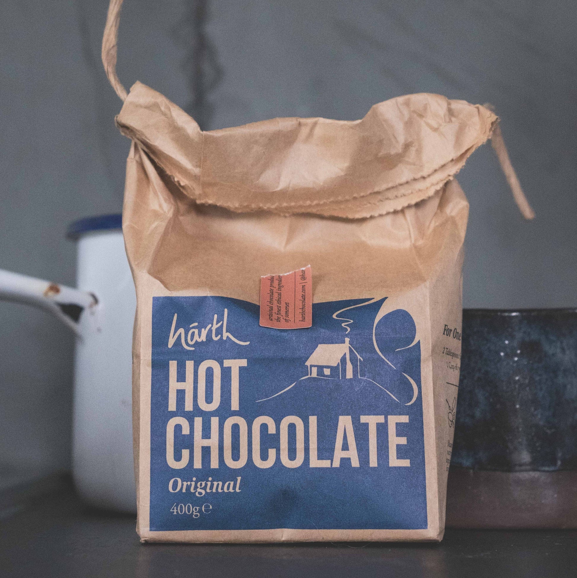 Brown paper bag of Harth Hot Chocolate with a blue label on a dark surface.