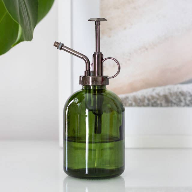 Green glass spray bottle with metallic nozzle on a white surface