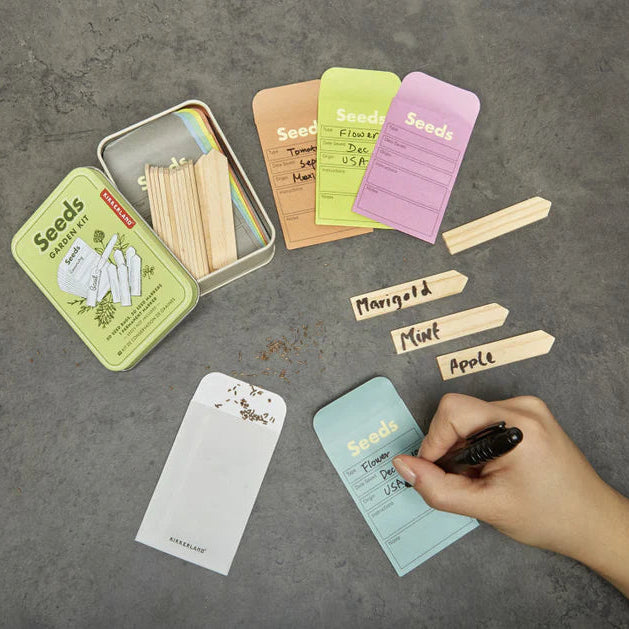 Set of seed packets and labels on a gray surface with a hand holding a pen.
