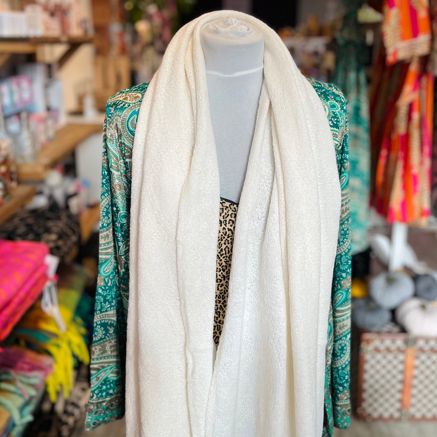 Mannequin wearing a white scarf with a colorful patterned garment in a store setting