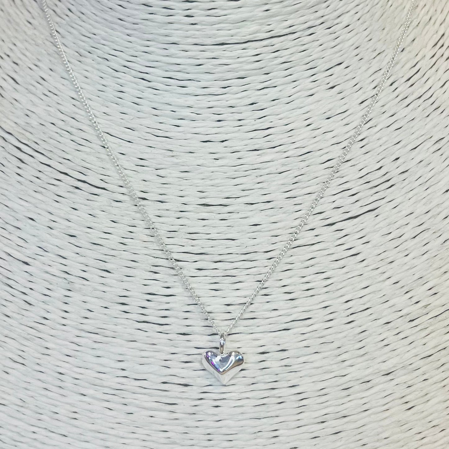 Silver heart-shaped pendant necklace on a textured beige background