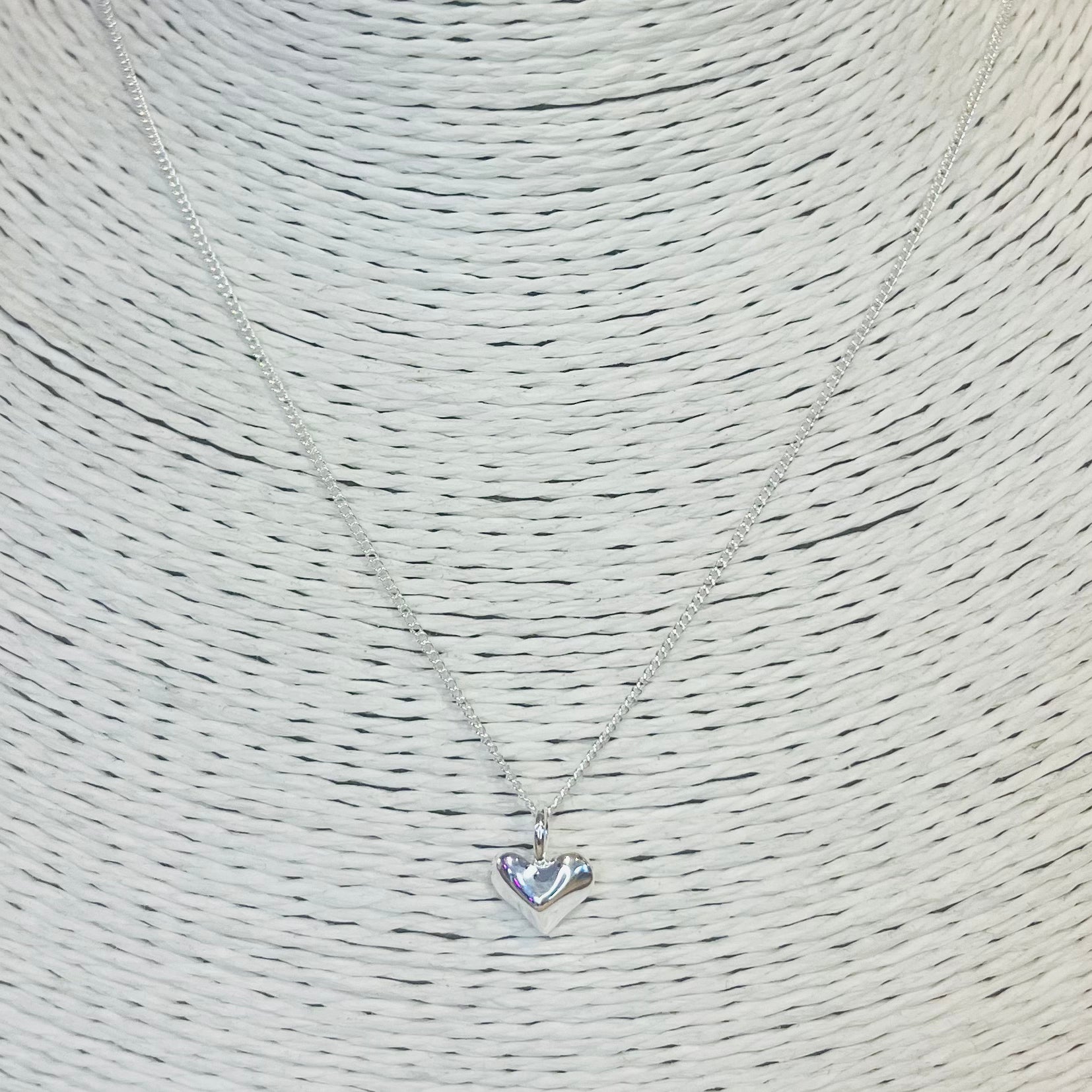 Silver heart-shaped pendant necklace on a textured beige background