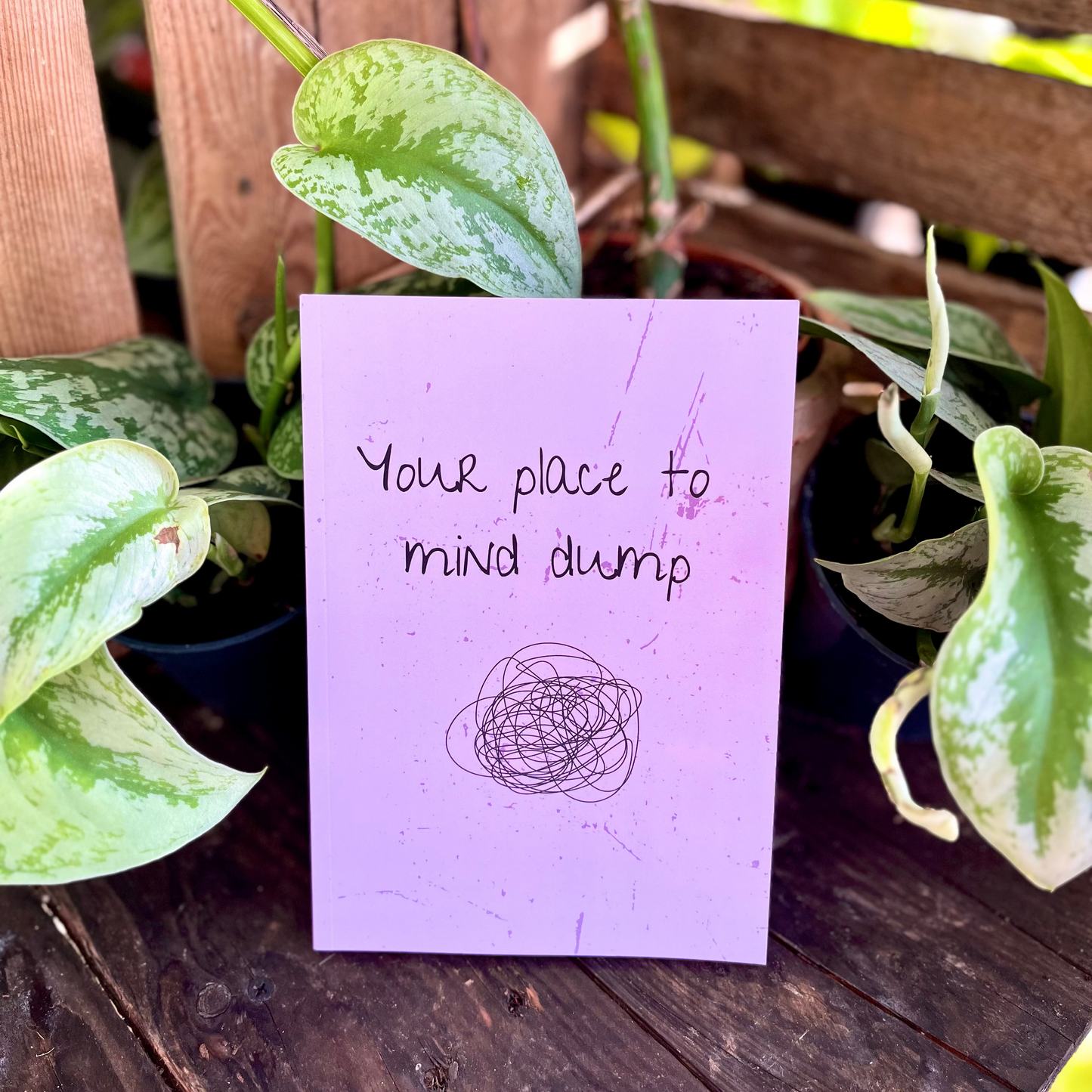 Purple card with text and a drawing on a wooden surface with plants in the background