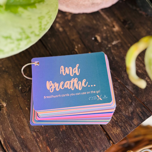 Stack of cards with 'And Breathe' text on a wooden surface with plants in the background
