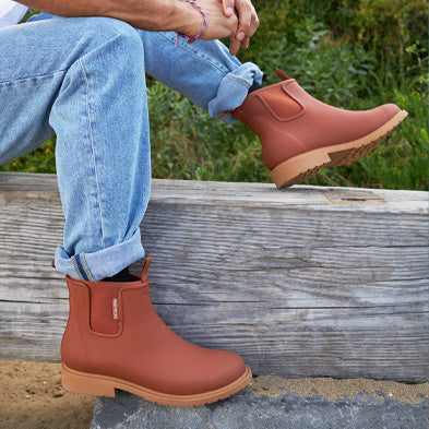 Person wearing brown ankle boots sitting on a wooden bench with a natural background