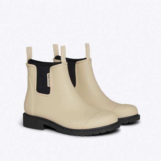 Pair of beige rubber boots with black soles on a white background