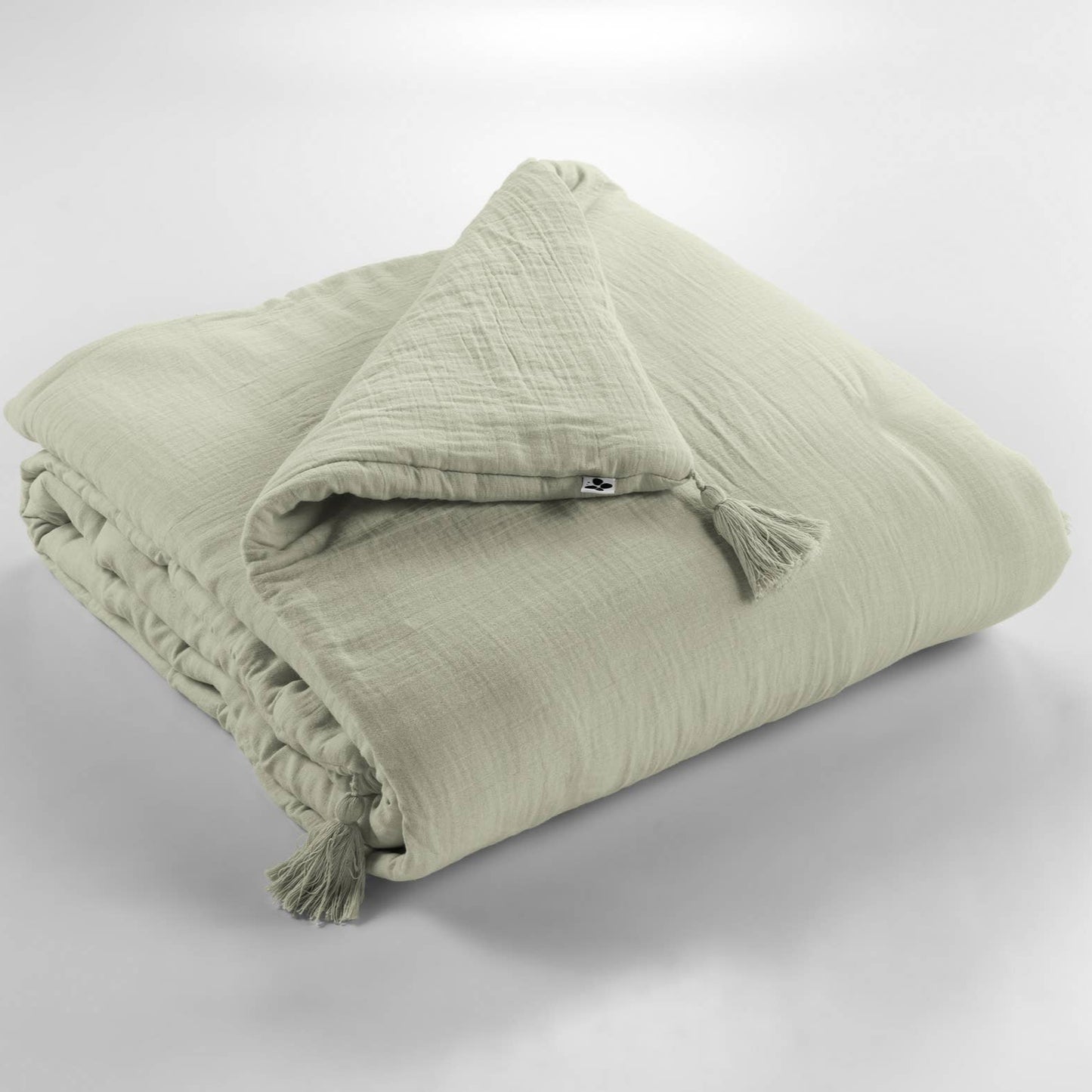 Folded green blanket with tassels on a light gray background