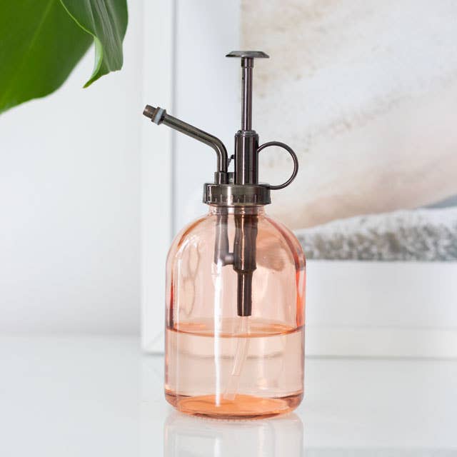 Pink glass spray bottle with bronze nozzle on a light background
