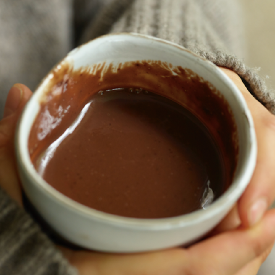 Person holding a small white bowl filled with a brown liquid, possibly hot chocolate.