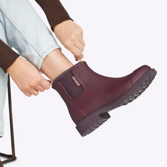Person putting on a maroon rain boot with a white background
