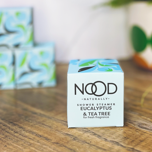 A small pale blue box with a floral pattern on the top, and branding for 'NOOD Naturally' printed on the side. The iteam has 'Eucalyptus & Tea Tree' 'shower steamer' written on it. 