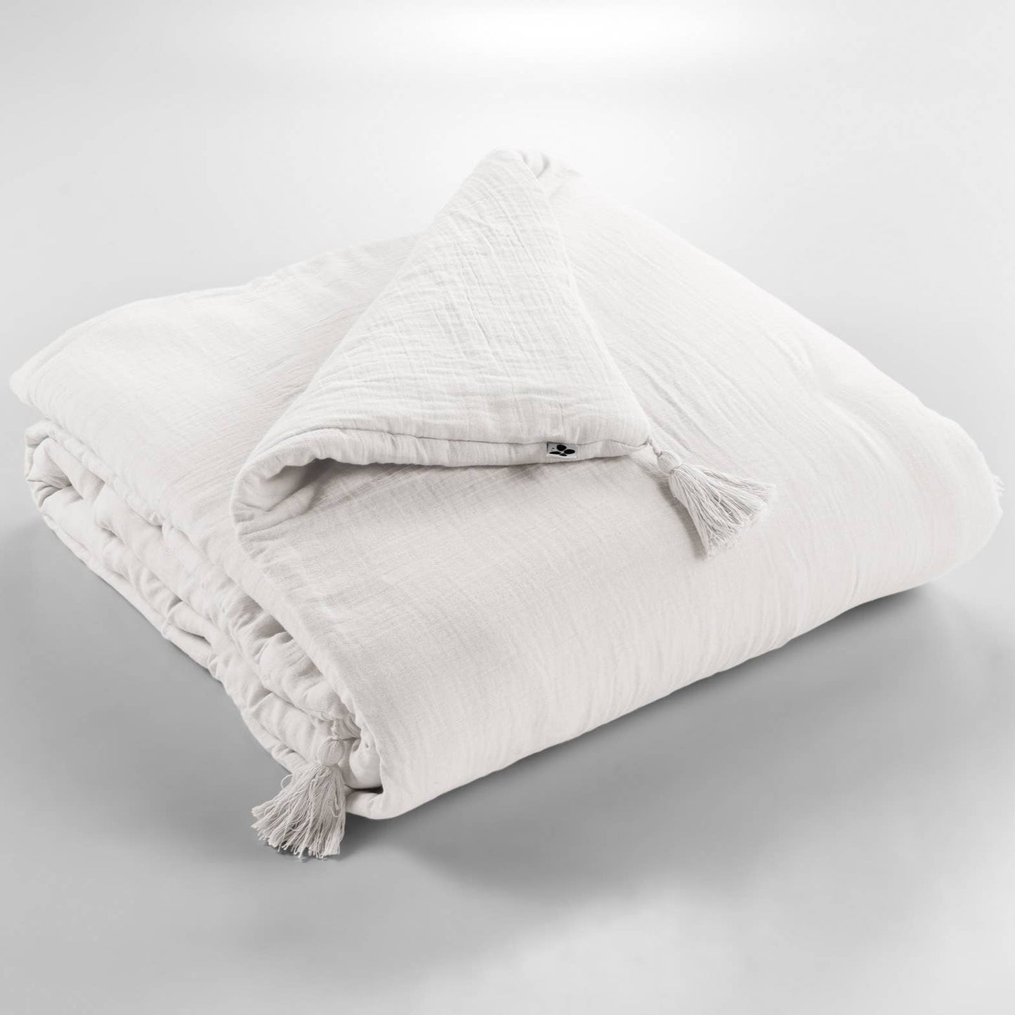 White textured blanket with tassels on a light gray background