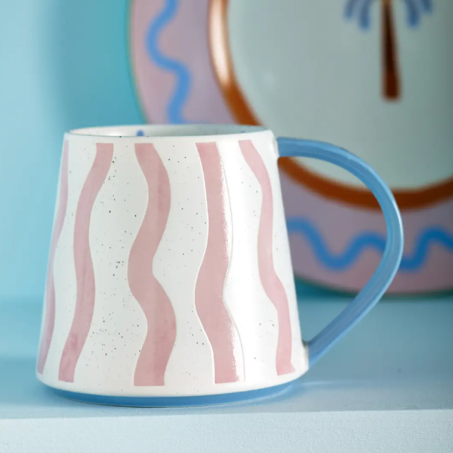 Ceramic mug with pink wavy patterns and blue handle on a light blue background