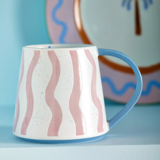 Ceramic mug with pink wavy patterns and blue handle on a light blue background